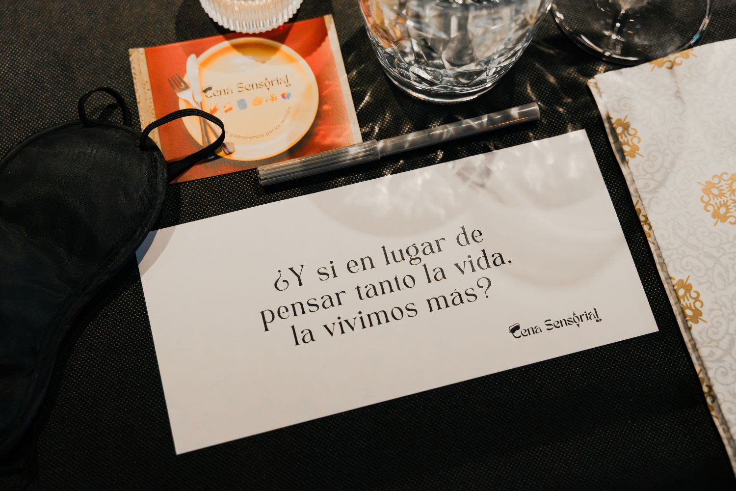 Tarjeta de La Cena Sensorial junto a un antifaz sobre la mesa